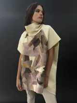 Poncho de lana merino afieltrada con cuello alto y mangas cortas. Diseño tipo mosaico con piezas geométricas en tonos verde azulado y gris.