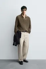 Polo de punto color marrón oscuro, de calce regular, con cuello solapa y abertura frontal en V. Presenta tejido con trencitas verticales.