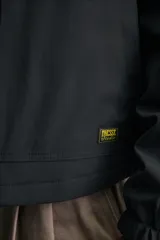 Cazadora técnica de corte holgado color negro, con cuello solapa, cierre frontal de cremallera metálica, bolsillos frontales ribeteados y puños con elástico.