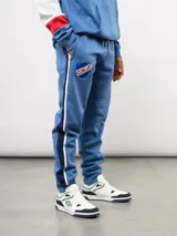 Pantalon de jogging azul de felpa, con franjas laterales en blanco y azul marino. Presenta el escudo del Club Nacional de Football en el muslo derecho y el logo de Umbro en el izquierdo.
