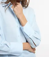 Camisa celeste de voile, corte oversized, con cuello clásico, cierre frontal con botones, mangas largas con puños largos y proceso de producción sostenible.