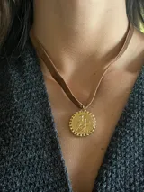 Collar tipo choker de cinta de terciopelo color tostado con dije circular dorado enchapado en oro 18k, con relieve de figura religiosa y borde texturado.
