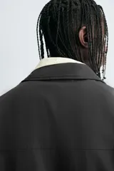 Sobrecamisa negra de algodón con estructura canvas, corte cropped y calce holgado. Presenta cuello solapa, manga larga, bolsillos laterales en cadera y cierre frontal con botones a presión metálicos.