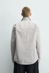 Camisa de corte slim fit confeccionada en tejido de algodón, con estampado de cuadros pequeños en tonos beige y blanco. Presenta cuello italiano, manga larga con puños abotonados y cierre frontal con botones.