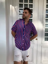 Camisa de seda con estampado de rayas verticales azules, rojas y blancas, con cuello clásico, manga corta con dobladillo y cierre frontal con botones blancos.