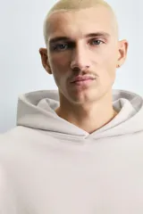 Sudadera tipo hoodie de color blanco hueso, con capucha, manga larga y bolsillo canguro frontal. Presenta un calce relajado y tejido de algodón con interior afelpado.