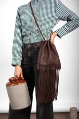 Cartera bandolera Dumpling Boho de cuero marrón, con diseño de silueta suave y relajada, cierre fruncido con cordones y flecos largos colgantes en la parte inferior. Incluye correa larga desmontable y bolsillos interiores.