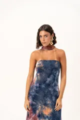 Vestido largo de corte recto y escote strapless, con estampado estilo batik en tonos azul, naranja y bordó. Incluye una bufanda larga integrada al diseño que cae desde el cuello.