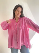 Camisa de algodón color rosa vibrante, con cuello mao y detalles de pliegues verticales en el frente. Presenta un calce holgado y mangas largas con puños abotonados.