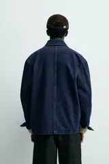 Chaqueta de denim de algodón en color azul oscuro con corte relaxed fit. Presenta cuello de solapa, cierre frontal con botones metálicos y tres bolsillos de parche en el delantero. Las mangas son largas con puños abotonados.