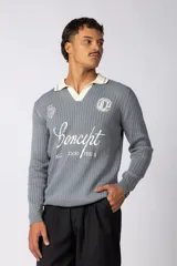 Sweater de punto acanalado color gris, con cuello polo en contraste color crema. Presenta bordados frontales con tipografía cursiva y logos circulares, de manga larga y calce regular.