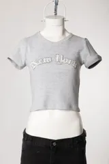 Remera de morley de manga corta, color gris, ajustada al cuerpo y elastizada, con bordado estilo college con la inscripción 'New York' en el pecho.