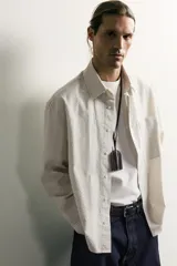 Camisa relaxed fit de algodón con estructura, cuello solapa, manga larga con puño abotonado, bolsillo de parche en el pecho y cierre frontal con botones. Presenta diseño de rayas finas.