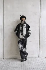 Campera unisex de cuello alto con cierre frontal completo. Presenta un diseño de paneles con efecto de lavado ácido en tonos negro y gris, corte relajado y bolsillos laterales.