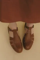 Sandalia cerrada tipo pescador de cuero negro charol, con tira en T y hebilla ajustable en el tobillo. Posee suela y taco bajo de madera.