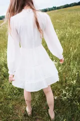 Vestido corto blanco con cuello mao de volados, mangas globo largas con puños fruncidos y falda escalonada con inserciones de encaje en escalera.