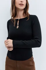 Sweater de punto acanalado color negro, de corte ajustado y manga larga. Presenta un escote redondo con una abertura frontal tipo gota decorada con botones joya.