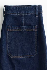 Jean de denim azul oscuro con tiro alto y piernas amplias de corte holgado. Cuenta con bolsillos delanteros de parche, cierre frontal con botón y raya marcada tanto en el frente como en la parte posterior.