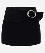 Short pollera mini de tiro bajo, confeccionado en bengalina negra. Presenta un diseño de cintura cruzada con detalle de hebilla ovalada metálica en el frente.