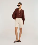 Bermuda de cintura mediana color beige, confeccionada en sarga, con trabillas, cierre tradicional, bolsillos y frisos delanteros. Incluye cinturón de tejido para lazo con hebilla metalizada.