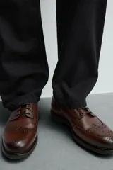 Zapato tipo derby de hombre, color marrón oscuro, fabricado en piel con detalles de picados (brogue) en puntera y laterales. Posee plantilla interior de piel y suela track con ligero tacón.