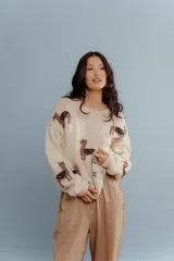 Sweater color crema tejido en lana merino con cuello redondo y mangas largas. Presenta diseño de llamas marrones con detalles en zigzag negros.