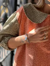 Blusa bicolor de pana elastizada con mangas cortas abullonadas, cuello redondo amplio y diseño estampado con combinación de tela roja con motivos florales pequeños y mangas y cuello en tono gris con estampa similar.