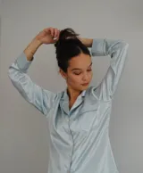 Camisa de satén elastizado color celeste, con cuello solapa, cierre frontal de botones y bolsillo en el pecho con detalle de vivo en contraste.