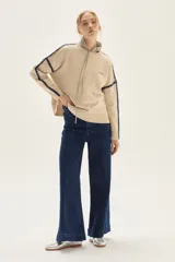 Sweater de tejido de punto color beige, con cuello redondo y detalles de bordado en zigzag en color azul oscuro a lo largo de las mangas y hombros. Presenta un pequeño bordado con texto en el pecho.