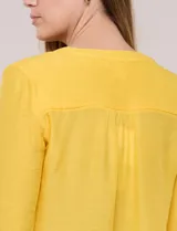 Blusa de calce relajado color salmón, confeccionada en tela liviana con textura sutil. Presenta escote en V con abotonadura frontal, bolsillo parche en el pecho, mangas largas regulables con presilla y ruedo con opción de anudar en el frente.