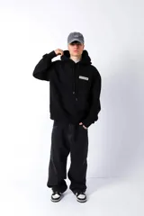 Hoodie negro de frisa con capucha y bolsillo canguro. Presenta un aplique rectangular en el pecho con texto en verde lima.