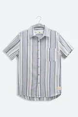Camisa de manga corta con rayas verticales en tonos azul, gris y blanco. Tiene cuello clásico, botones de coco y un bolsillo en el pecho.