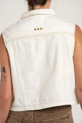 Chaleco de denim blanco sin mangas, con cuello camisero, bolsillos frontales plaqué con solapa y cierre frontal de botones con detalles de costuras onduladas en contraste.