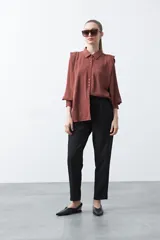 Camisa negra de estilo sastrero con cuello clásico, frente abotonado y mangas largas con puños ajustados. Presenta un diseño con hombreras sutiles que aportan estructura a la prenda.