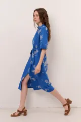 Vestido midi azul con estampado floral blanco, cuello en V, mangas cortas abullonadas y cierre frontal de botones. Incluye un lazo ajustable para la cintura.