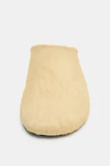 Zapato tipo mule de mujer confeccionado en piel con textura de pelo en color beige. Presenta un diseño de punta redonda y suela plana en contraste.