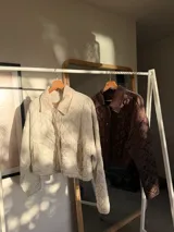Chaqueta corta de color marrón con diseño acolchado de rombos, cuello camisero y cierre frontal con botones a presión.