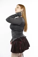 Top de manga larga color negro, confeccionado en jersey elástico. Presenta un diseño asimétrico con jaretas laterales regulables que permiten ajustar el largo y el volumen, y aberturas para los pulgares en los puños.