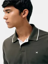 Remera polo blanca de manga corta, con cuello camisero y ribetes grises en cuello y puños. Cuenta con cierre frontal de botones y un pequeño logo bordado en el pecho.