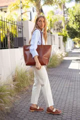 Bolso tote de cuero color tostado con costuras blancas a la vista en los laterales y doble asa de hombro.