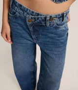 Pantalón wide leg de tiro medio confeccionado en denim de algodón. Presenta un diseño de cintura cruzada con cierre tradicional, trabillas para cinturón y bolsillos funcionales.