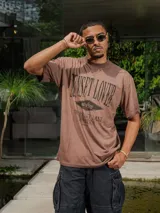 Remera de jersey con efecto teñido, color marrón, de corte holgado y cuello redondo. Presenta un estampado frontal con texto en tonos más oscuros.