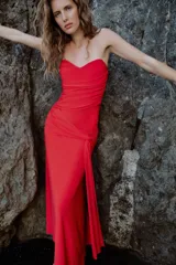 Vestido largo de fiesta color rojo, con escote corazón y diseño palabra de honor. Presenta detalles de drapeado lateral y una superposición de tela con lazada en la cintura, con falda de corte evasé.