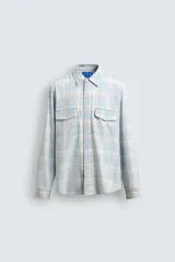 Camisa de algodón con efecto lavado, diseño a cuadros en tonos celestes y beige, cuello solapa, manga larga con puños abotonados y bolsillos frontales con solapa.