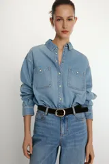 Camisa de denim de corte oversize con cuello solapa, manga larga con puños, cierre frontal con botones a presión y bolsillos de plastrón en el delantero.