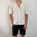 Camisa de tejido de punto calado color negro, con cuello solapa, cierre frontal de botones y mangas cortas.