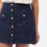 Falda corta de denim azul oscuro, con cierre frontal de botones metálicos dorados y dos bolsillos frontales tipo parche.