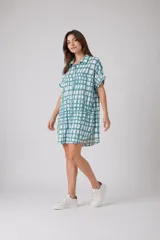 Vestido camisero de corte holgado y silueta relajada, con cuello clásico, cierre frontal de botones y mangas cortas con dobladillo. Presenta un estampado de cuadros irregulares en color bordó sobre fondo blanco.