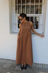 Vestido largo color marrón, sin mangas, con escote redondo, espalda con leve abertura, bolsillos laterales y logo bordado en dorado en el frente.