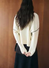 Chaleco de punto color blanco con detalles de líneas negras en los hombros y sisas, cuello alto y diseño holgado.